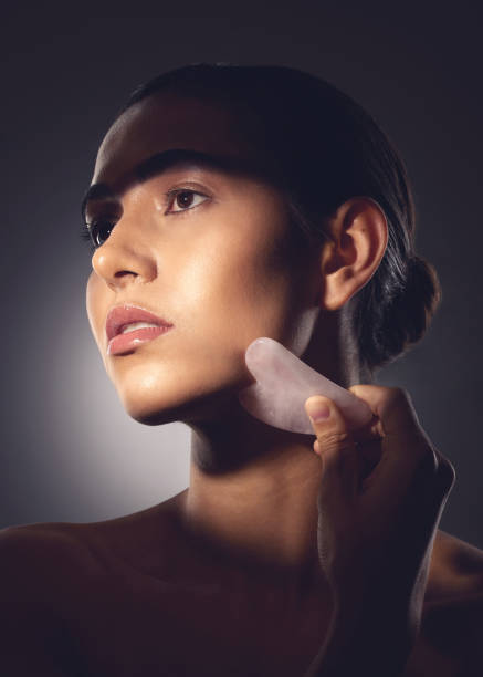 foto de estudio de una mujer usando una herramienta de raspado facial en su cara - spooning fotografías e imágenes de stock