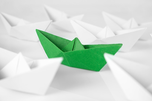 Green paper boat with white paper boats on white background
