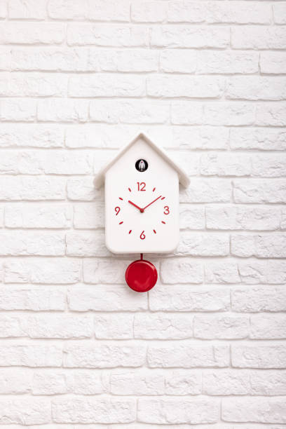 istock Cuckoo bird clock with red pendulum on a white brick wall 1387164740