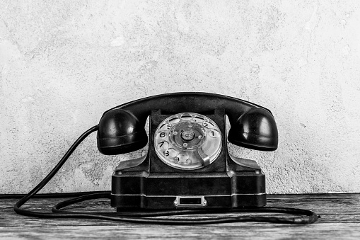 Retro black rotary telephone on wooden table in front gray concrete background