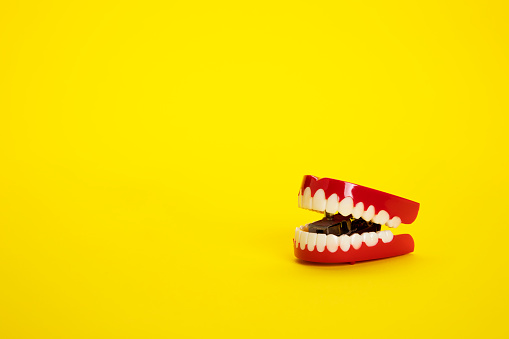 This is a photograph of chattering teeth on a yellow background with space for copy