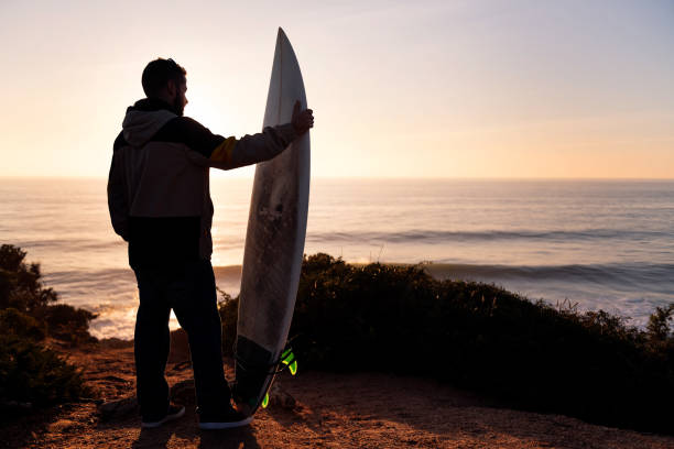 istock man looking at the sea at sunset with a surfboard 1387172593