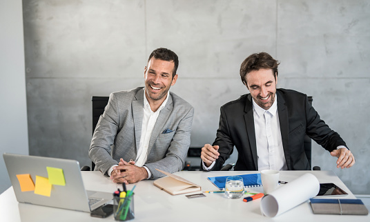 Two cheerful young businessmen taking a break from work and laughing.