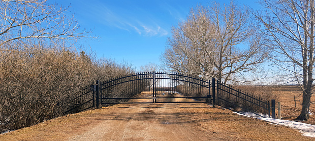 Large Black iron gate across driveway in rural countryside.
