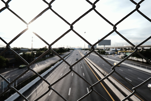 Transport and logistics industry. Wire mesh fence with highway background. Motorway in the city. Road travel.
