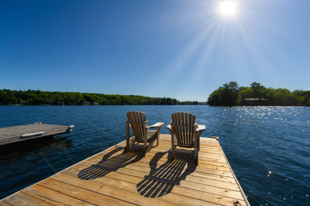 Sunrise on two empty Adirondack chairs Cottage life - Sunrise on two empty Adirondack chairs sitting on a dock on a lake in Muskoka, Ontario Canada. The sun light create long shadows on the wooden pier. promenade stock pictures, royalty-free photos & images