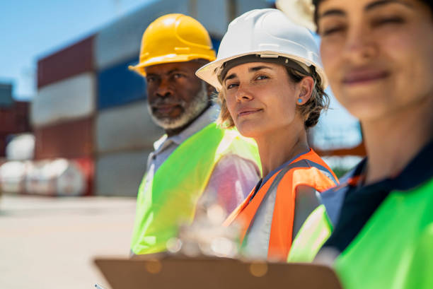 istock Female dock worker standing between coworkers at shipping yard while looking at the camera 1387192013