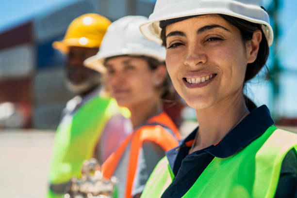 istock Female dock worker standing next to coworkers at shipping yard while looking and smiling at the camera 1387192022