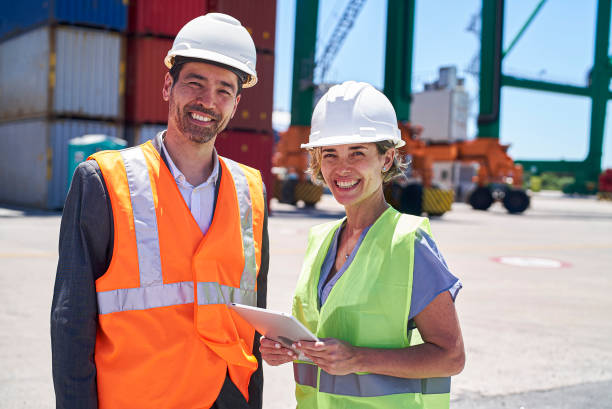 istock Dock control coworkers looking at the camera while hiolding digital tablet standing at shipping yard 1387192031