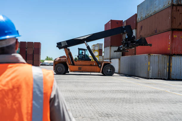 istock Male foreman dock worker looking at parked forklift at shipping yard 1387192929