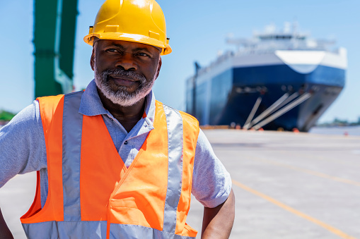 Front view of african american male dock worker standing with hands on waist at shipping yard during daytime