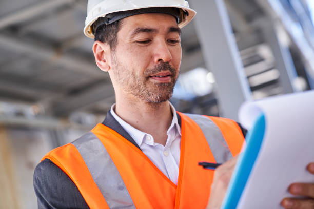istock Asian american male supervisor taking notes on clipboard while standing on shipping container yard 1387193123