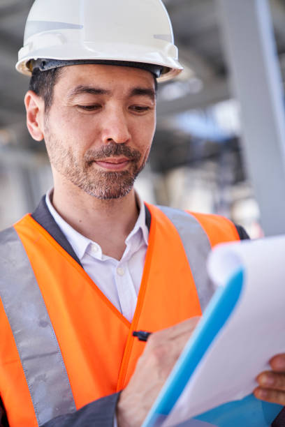 istock Asian american male supervisor taking notes on clipboard while standing on shipping container yard 1387193129
