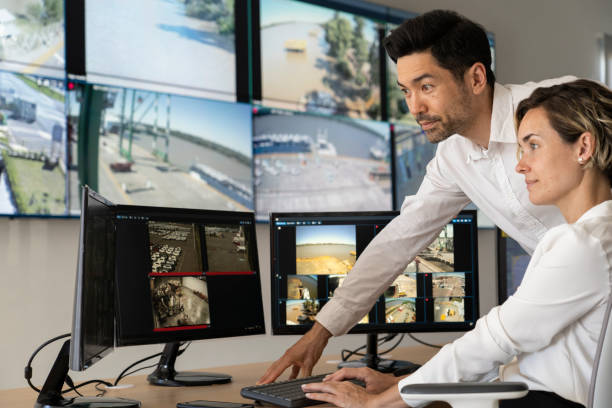 Male and female security coworkers watching monitors at control room stock photo