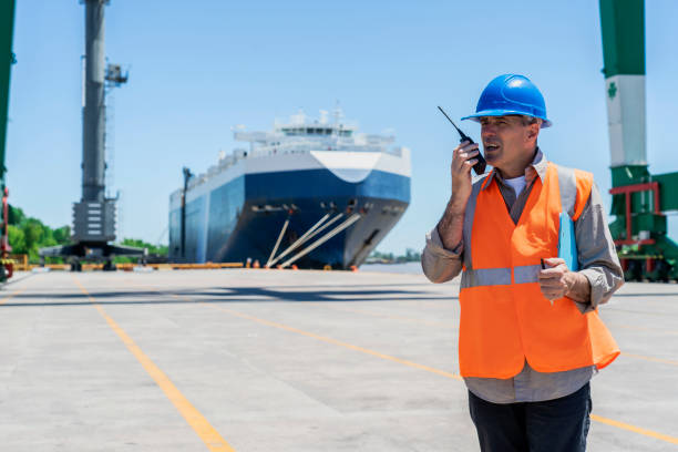istock Male cargo handler talking on walkie talkie while standing at shipping yard 1387193214