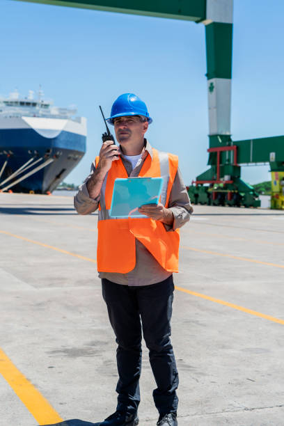 istock Male cargo handler using walkie talkie while standing at shipping yard 1387193220