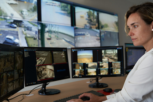 Side view of adult female security worker watching monitors at control room