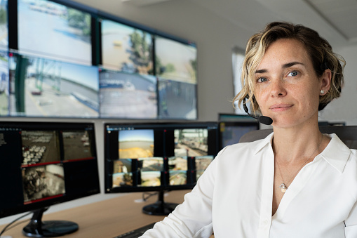 Front view of adult female security worker wearing headset while looking at the camera at control room