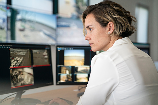 Side view of adult female security guard looking carefully at computer screen at surveillance control