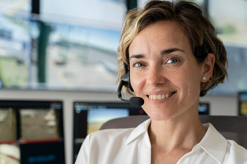 Front view of adult female security worker looking at the camera while using wireless headset at control room