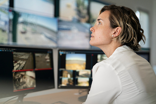 Side view of adult female security guard sitting at desk while looking at video wall