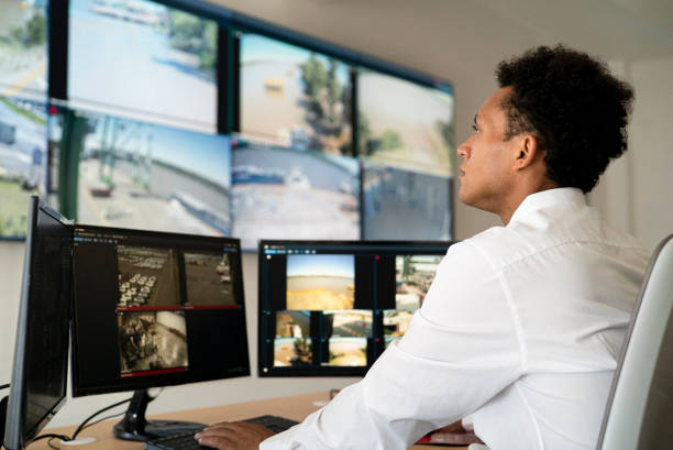 trabajador de seguridad masculino adulto joven viendo video wall mientras está sentado en el escritorio - security camera security system surveillance security fotografías e imágenes de stock