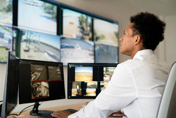 Young adult male security worker watching video wall while sitting at desk stock photo