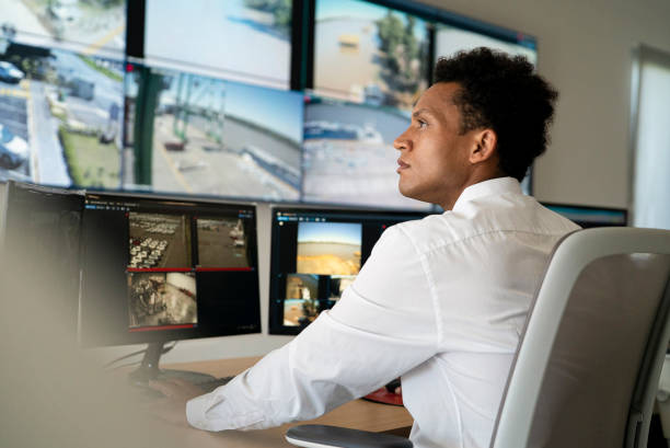 istock Young adult male security worker watching video wall while sitting at desk 1387193295