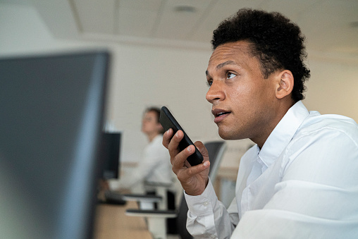 Side view of young adult male security worker using smart phone while sitting at desk in control room