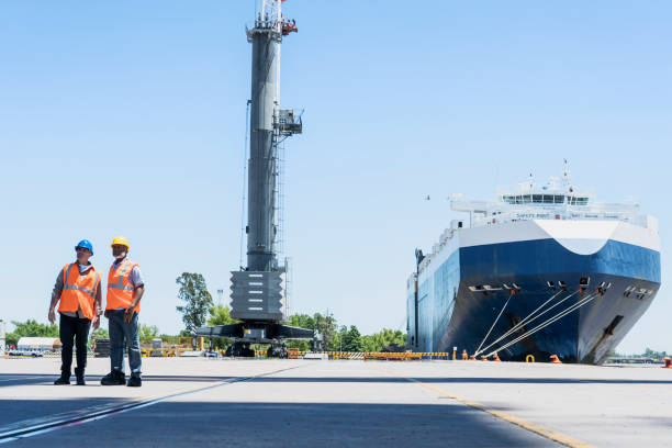 istock Male foreman engineer and dock worker standing on shipping yard 1387193318