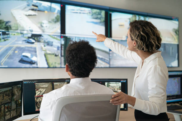 Female and male security coworkers discussing while looking at video wall Rear view of female and male security coworkers discussing while looking and pointing at video wall in control room control room stock pictures, royalty-free photos & images