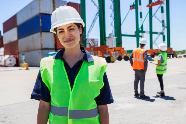 trabajadora de control portuario mirando la cámara mientras sus compañeros de trabajo están de pie en el fondo - industrial ship dock worker engineer harbor fotografías e imágenes de stock