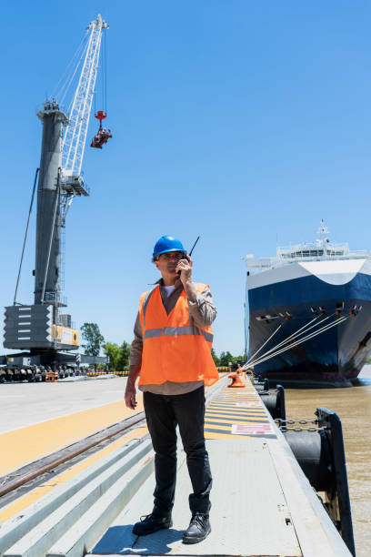Male cargo handler talking on walkie talkie while standing on ship dock