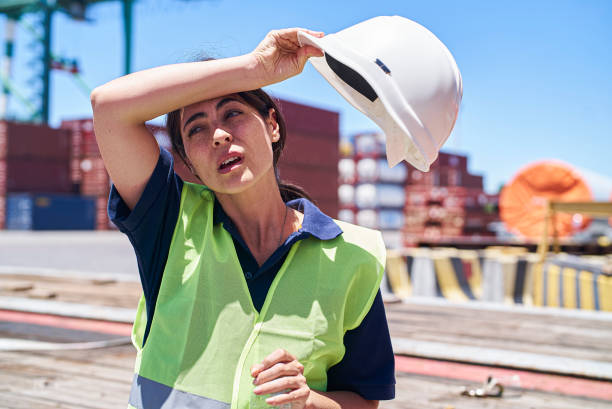 Female dock worker holding plastic bottle while wiping sweat with arm
