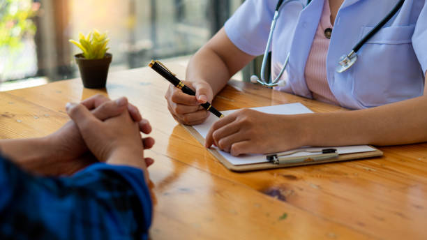 young man talking to a female doctor in clinic close-up of patient and doctor taking notes, doctor closely consulting patient's hand patient sitting at the doctor's office - department of health and human services imagens e fotografias de stock