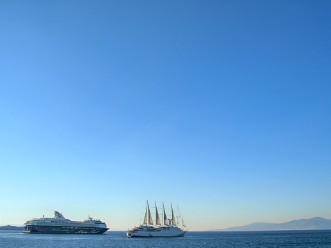 Ships passing in Mykonos Harbour in the late afternoon. The ship with sails is moored and the other is sailing past. This image was taken in autumn.