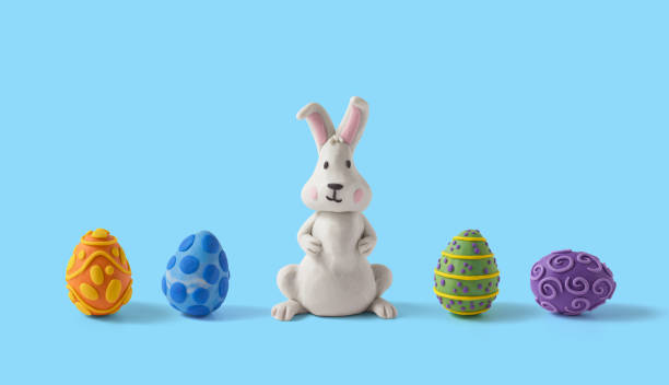 istock Easter greeting card with rabbit design and easter eggs lined up and centered. Handmade from plasticine on a blue background with copy space 1387200128