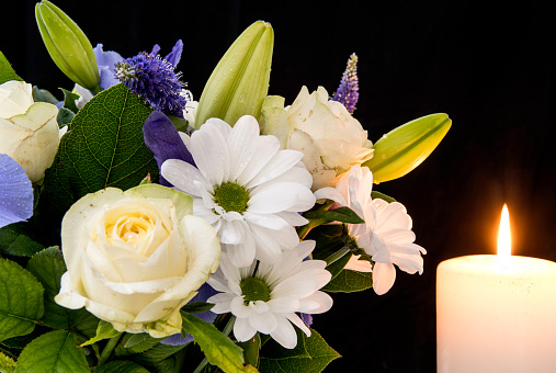 Funeral Bouquet purple White flowers and burning white candle, Sympathy and Condolence Concept on black background with copy space.