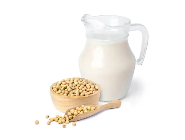 Soymilk in glass jug with soy bean in wooden bowl isolated on white background.
