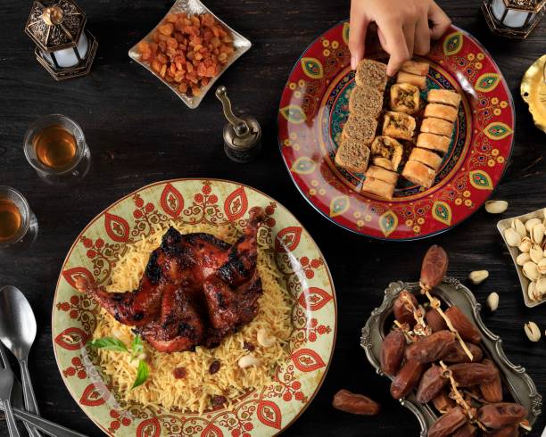 istock Female Hand Pick Turkish Baklava on Plate, Table Setting for Ramazan Greeting with Dates Fruit, Arabian Rice, ROasted CHicken, Nuts, and Tea. 1387216942