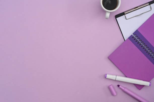 Top view notebook, clipboard and coffee cup on purple background with copy space.