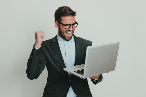 Happy and ecstatic young businessman using a laptop and celebrating a win, studio shoot in front of a white background