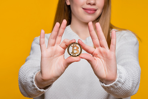 Faceless woman in white sweater holding golden bitcoin, advertise of digital money btc coin for e-commerce. Hands unrecognizable girl hold golden bitcoin. Cryptocurrency, blockchain, tokens and nft.