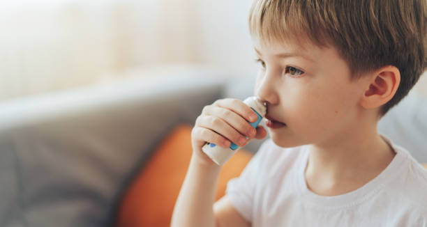 маленький мальчик использует назальный спрей, сидя на диване - nasal spray allergy bottle body care стоковые фото и изображения