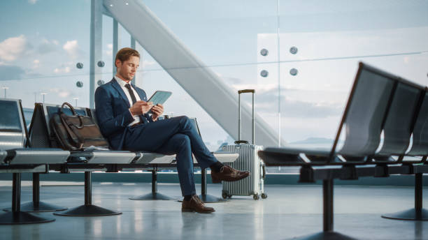 istock Airport Terminal Flight Wait: Smiling Businessman Uses Digital Tablet Computer for e-Business, Browsing Internet with App. Traveling Entrepreneur Work Online, Sitting in Boarding Lounge of Airline Hub 1387222162