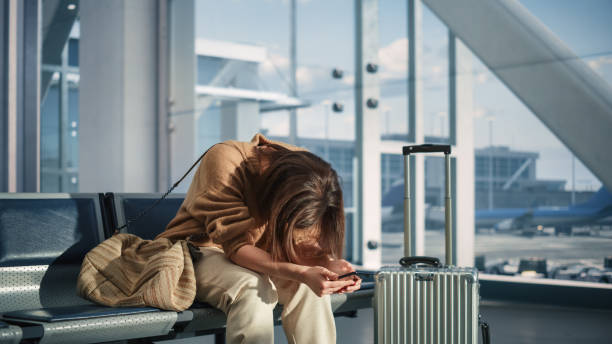 terminal de l’aéroport: une femme attend son vol, utilise un smartphone, reçoit de mauvaises nouvelles, se met à pleurer. une personne bouleversée, triste et déçue manque son vol alors qu’elle est assise dans une salle d’embarquement d’un hub - salle dembarquement photos et images de collection