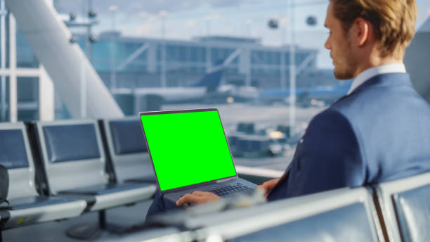 terminal de l’aéroport: homme d’affaires travaillant sur un ordinateur portable à écran green chroma key en attendant son vol en avion. entrepreneur fait du travail à distance en ligne dans la salle d’embarquement du hub aérien. par-dessus l’� - salle dembarquement photos et images de collection