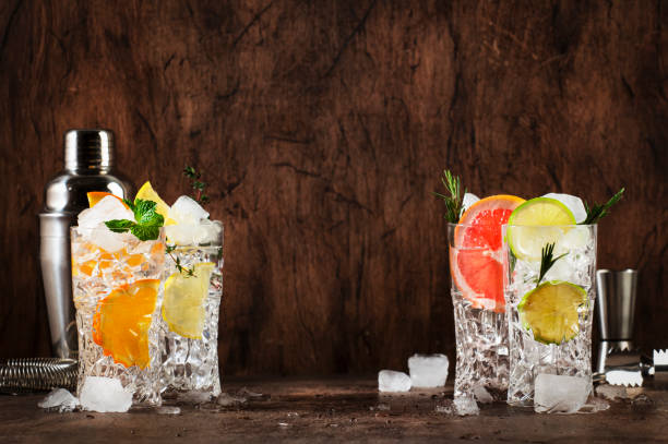 istock Gin tonic and citrus cocktails set. Summer drinks with lime, lemon, grapefruit, orange, soda and herbs in highball glasses, wooden counter background, cocktail party 1387222724