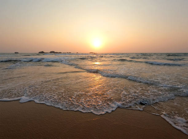 istock Soft blue ocean waves on a clean sandy beach at sunset. 1387225084