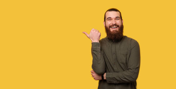 istock Panorama portrait of a bearded man pointing with the thumb over backdrop. 1387226166